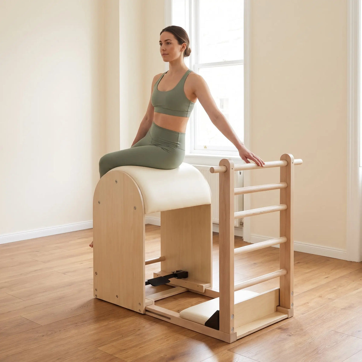 Frau sitzt seitlich auf dem Fass des Elina Pilates Elite Ladder Barrel, eine Hand auf der Sprosse