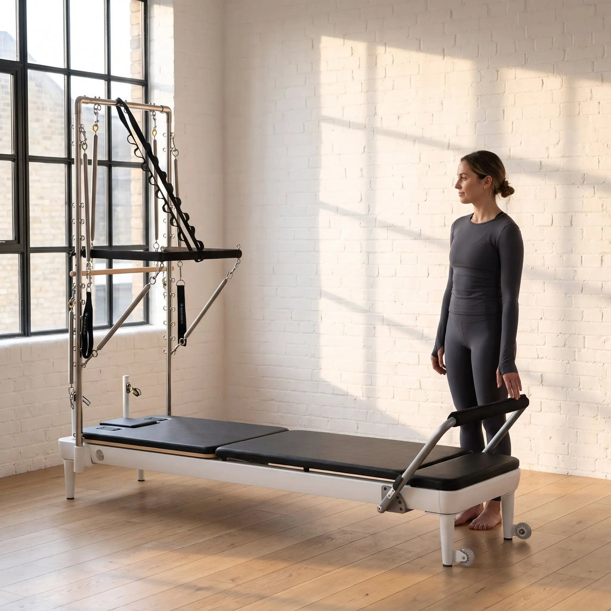 Trainerin steht am Fußende des Elina Pilates Nubium mit Tower in einem Loft-Studio