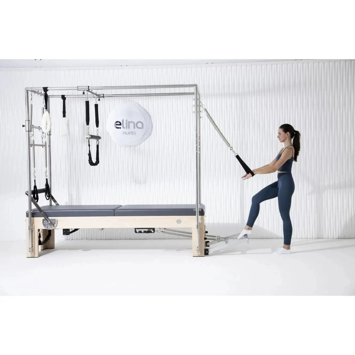 Elina Pilates Cadillac Elite Reformer aus Rock-Ahorn – Frau trainiert stehend mit Schlaufe am Rahmen im Studio