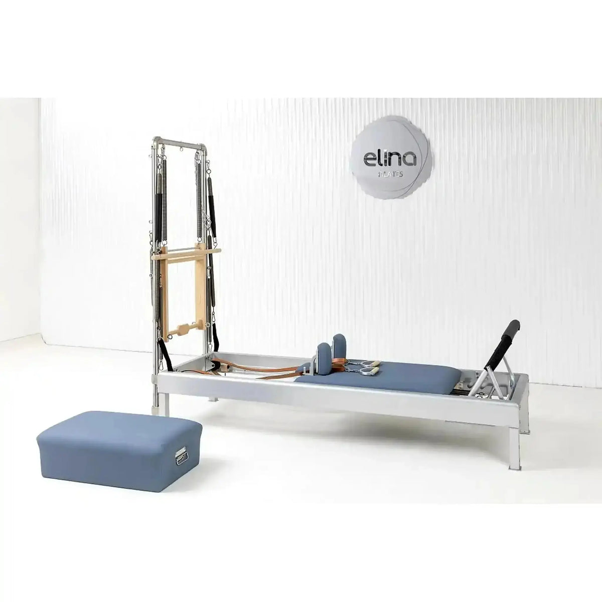 Elina Pilates Classic Reformer mit Tower aus Aluminium – im Studio vor weißer Wand mit blauem Polster und Sitzbox