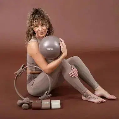 Elina Pilates Pilates-Ring in Taupe, Frau sitzt am Boden mit Ring und Pilates-Ball vor braunem Hintergrund
