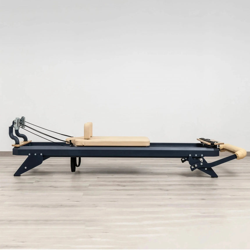 Side view of the HEGREN TALMA 62 Pilates Reformer showcasing its steel frame and beige upholstery.