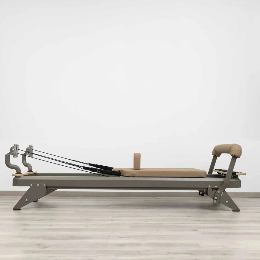 Side view of the HEGREN TALMA 62 Pilates Reformer showcasing its steel frame and beige upholstery.