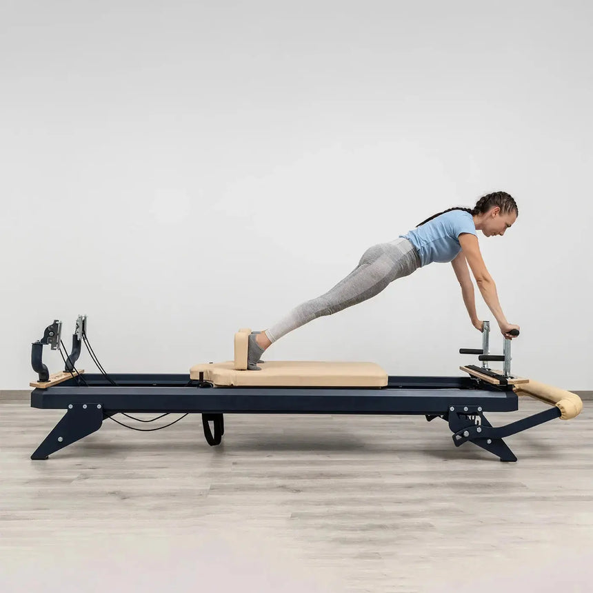 Side view of the HEGREN TALMA 62 Pilates Reformer showcasing its steel frame and beige upholstery.