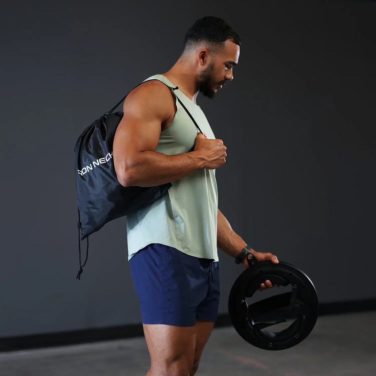 Mann mit Turnbeutel aus dem Iron Neck Strength Kit Band-Set über der Schulter, Nackentrainer in der Hand