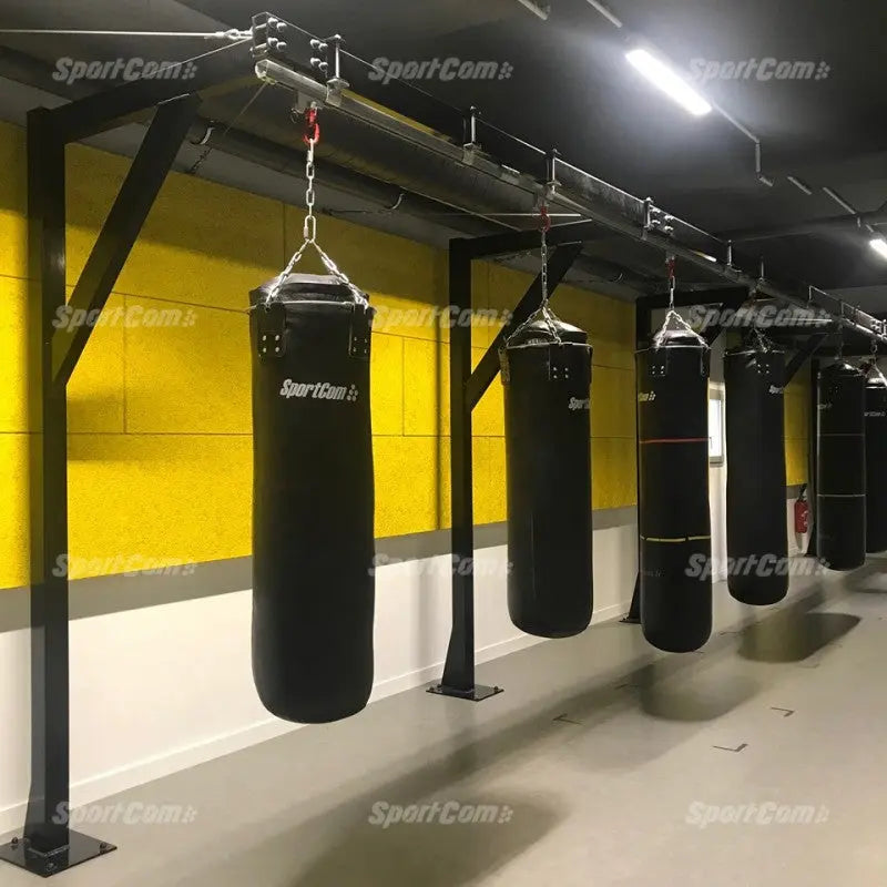 SportCom Förderschiene mit Rahmen für Sandsäcke, in einem Gym mit gelber Wand und schwarzen Sandsäcken