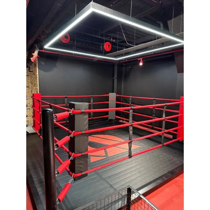 SportCom Freistehender Boxring mit roten Seilen und schwarzen Eckpfosten in einem dunklen Kampfsportstudio