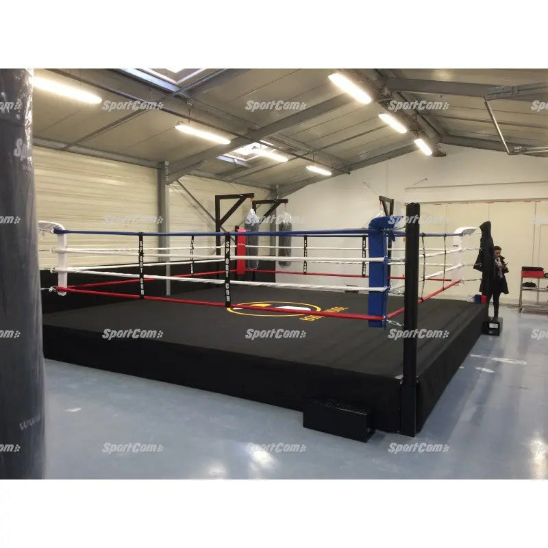 SportCom Pro-Trainingsboxring mit 50 cm Podium, in einer Halle mit blauer Ecke und Logo