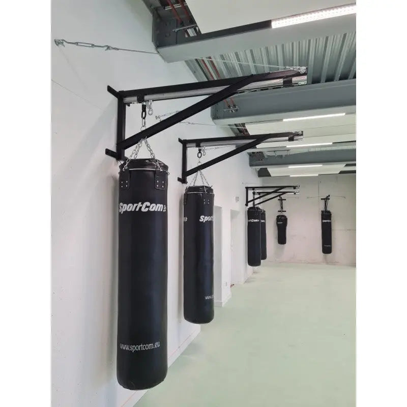 SportCom Sandsack-Wandhalterung mit Schiene und Laufwagen in Reihe an einer hellen Wand mit schwarzen Sandsäcken
