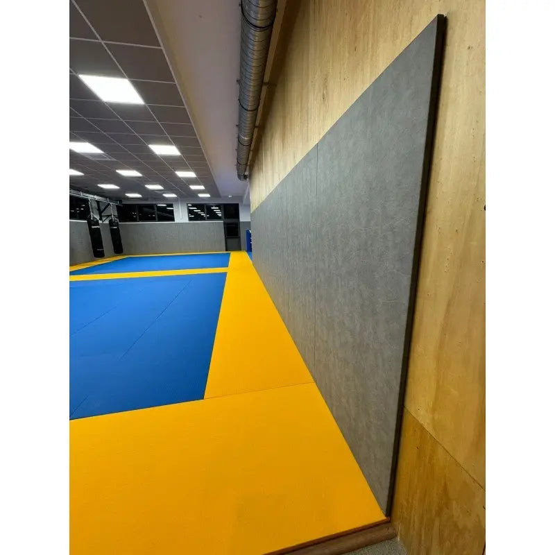 SportCom Wandpolster Standard, graues Polster an Holzwand neben blau-gelben Matten