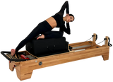 Woman using a Pilates reformer machine on a white background