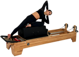 Woman using a Pilates reformer machine on a white background