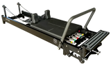 Body & Exercise Reformer Black Edition in Schrägansicht mit Fußstange, farbigen Federn und Schulterstützen in Schwarz