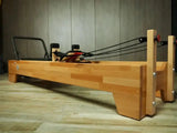 Body & Exercise Reformer Studio P001 aus Buchenholz, Seitenansicht mit Seilen in einem Raum mit Holzboden