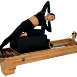 Body & Exercise Reformer Studio P001 aus Buchenholz, Frau bei einer Übung auf dem Reformer, schwarzer Hintergrund