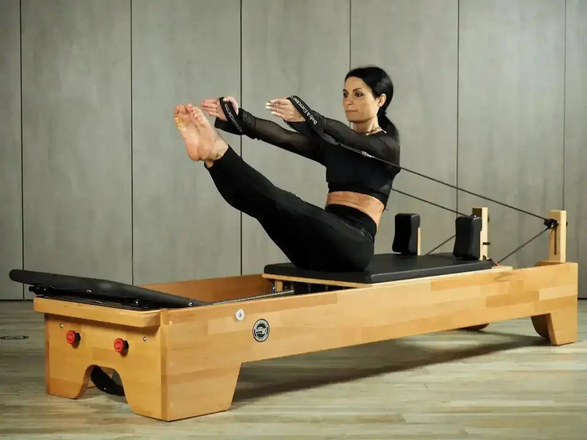 Body & Exercise Reformer Studio P001 aus Buchenholz, Frau bei einer Übung mit den Schlaufen im Studio