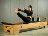 Body & Exercise Reformer Studio P001 aus Buchenholz, Frau bei einer Übung mit den Schlaufen im Studio