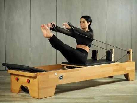 Body & Exercise Reformer Studio P001 aus Buchenholz, Frau bei einer Übung mit den Schlaufen im Studio