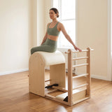 Frau sitzt seitlich auf dem Fass des Elina Pilates Elite Ladder Barrel, eine Hand auf der Sprosse