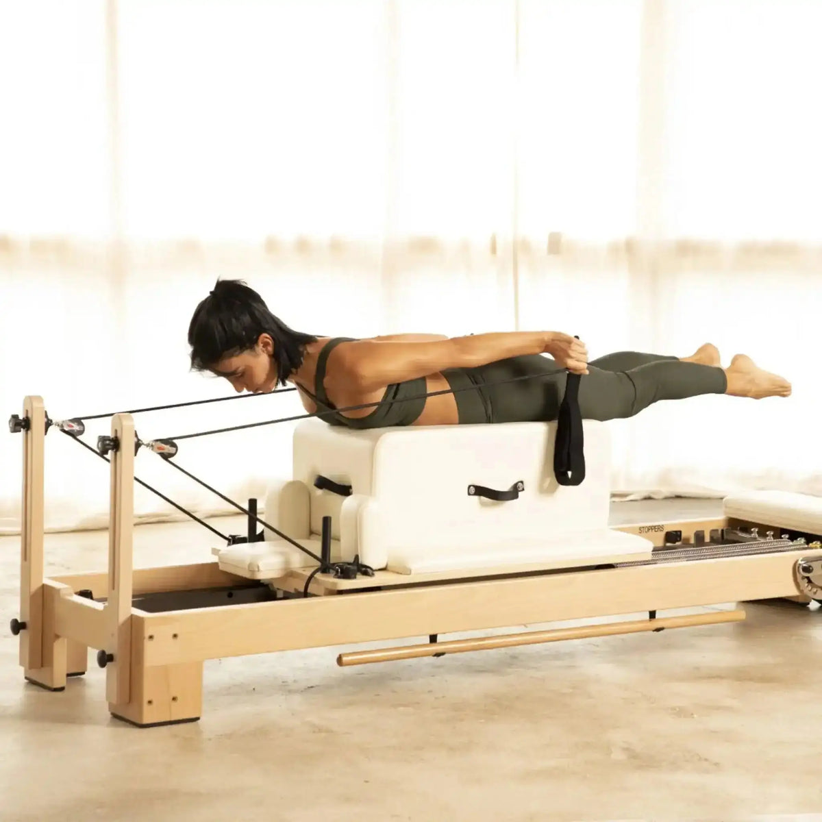 Frau liegt bäuchlings auf der Sitzbox des Elina Pilates Lignum Reformers