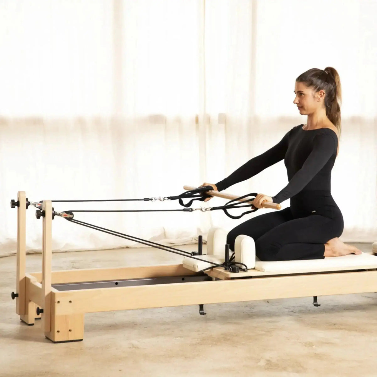 Frau kniet auf dem Elina Pilates Lignum Reformer und zieht die Seilschlaufen