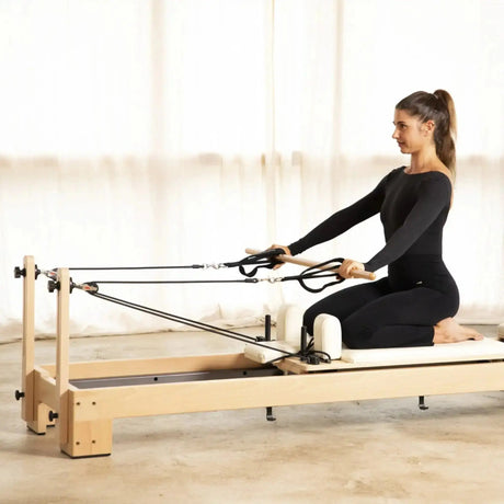 Frau kniet auf dem Elina Pilates Lignum Reformer und zieht die Seilschlaufen