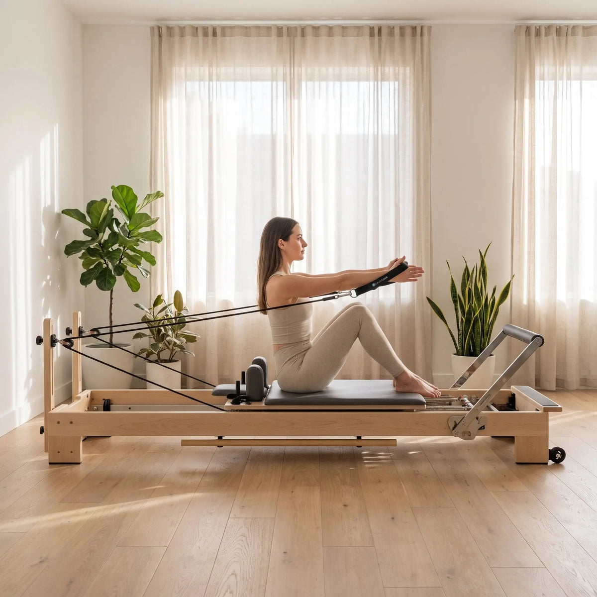 Frau sitzt auf dem Elina Pilates Lignum Reformer und zieht die Seilschlaufen in einem hellen Studio