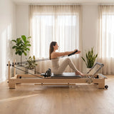 Frau sitzt auf dem Elina Pilates Lignum Reformer und zieht die Seilschlaufen in einem hellen Studio