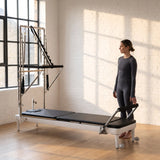 Trainerin steht am Fußende des Elina Pilates Nubium mit Tower in einem Loft-Studio