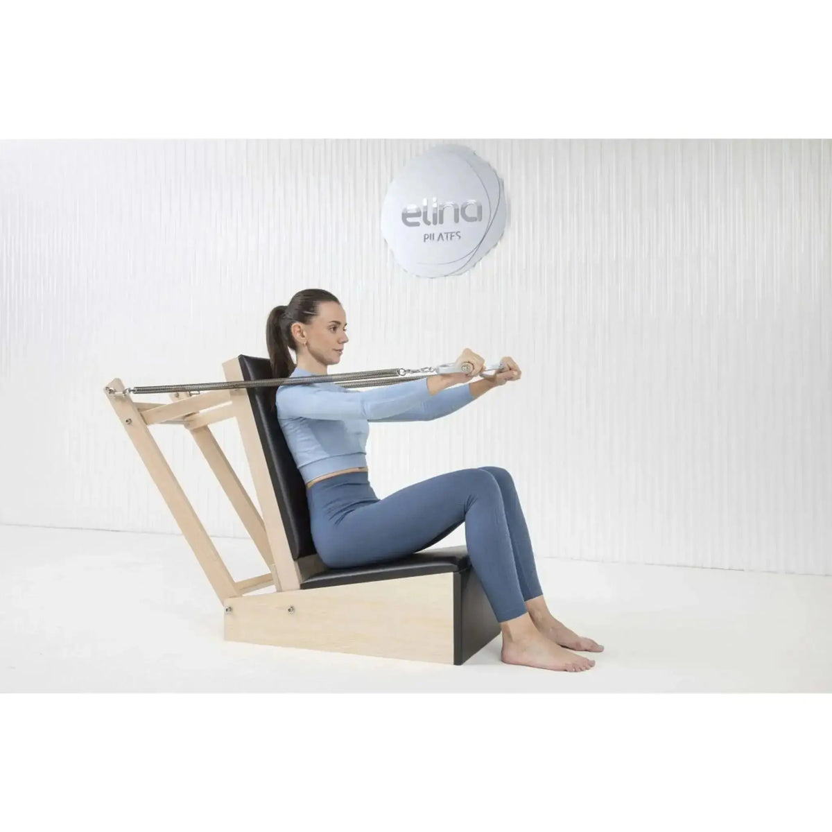 Elina Pilates Baby Chair aus Ahornholz: Frau sitzt und zieht die Griffe nach vorn, Seitenansicht