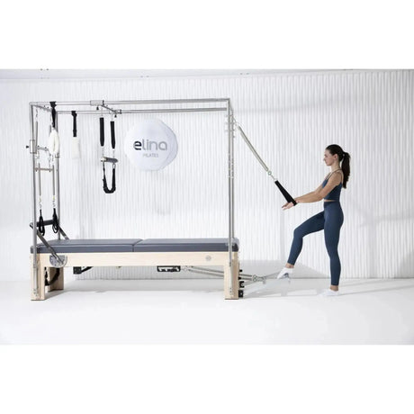 Elina Pilates Cadillac Elite Reformer aus Rock-Ahorn – Frau trainiert stehend mit Schlaufe am Rahmen im Studio