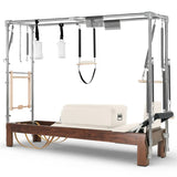 Elina Pilates Cadillac Reformer aus Walnussholz – Schrägansicht mit Stahlrahmen und Polstern in Altrosa, Elfenbein