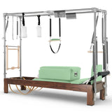 Elina Pilates Cadillac Reformer aus Walnussholz – Schrägansicht mit Stahlrahmen und Polstern in Eukalyptus, Grün