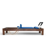 Elina Pilates Classic Reformer aus Walnussholz mit Polstern in Blau, Seitenansicht vor weißem Hintergrund