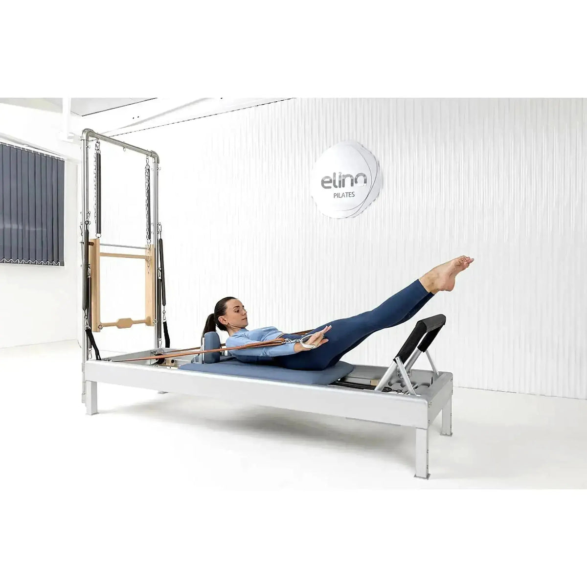 Elina Pilates Classic Reformer mit Tower aus Aluminium – Frau in Rückenlage mit gestreckten Beinen im Studio