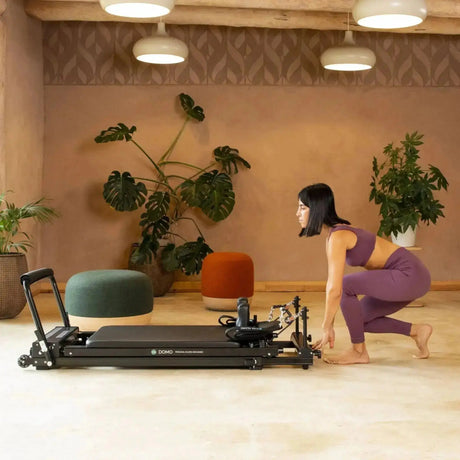 Elina Pilates Domo Reformer aus Aluminium im Studio, eine Frau kniet neben dem Gerät am Boden