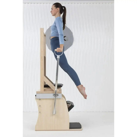 Elina Pilates Electric Chair Kombi-Wunda aus Ahornholz: Frau stützt sich auf die Griffe und streckt ein Bein nach hinten