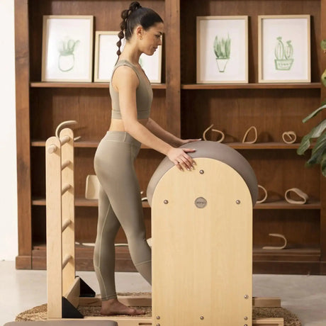 Elina Pilates Ladder Barrel mit Holzbasis im Wohnraum, Frau steht auf der Basis vor dem Barrel