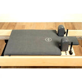 Elina Pilates Machine Towel Reformer-Handtuch in Grau auf dem Liegewagen eines Holz-Reformers, Schrägansicht mit Schulterstützen