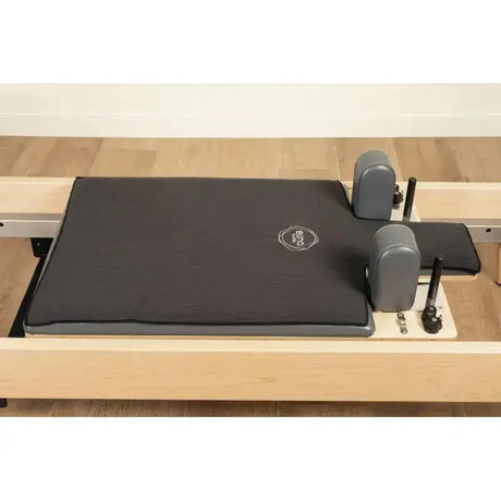 Elina Pilates Machine Towel Reformer-Handtuch in Schwarz auf dem Liegewagen eines Holz-Reformers, Schrägansicht mit Schulterstützen