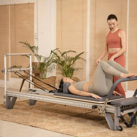 Elina Pilates Mentor Reformer aus Aluminium, Frau trainiert in Rückenlage mit Trainerin im Studio