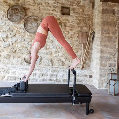 Elina Pilates Nubium Black Edition Reformer aus schwarzem Aluminium im Steinraum, Frau im Stand auf dem Schlitten
