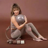Elina Pilates Pilates-Ring in Taupe, Frau sitzt am Boden mit Ring und Pilates-Ball vor braunem Hintergrund