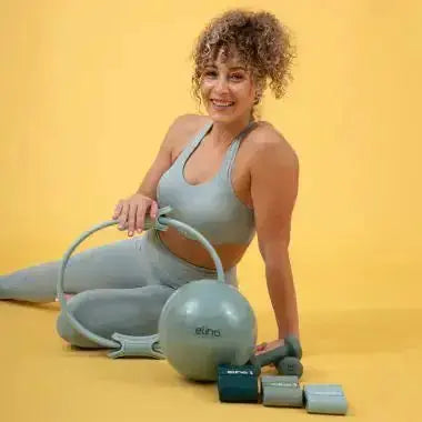 Elina Pilates Pilates-Ring in Hellblau, Frau sitzt am Boden mit Ring, Pilates-Ball und Gewichten vor gelbem Hintergrund