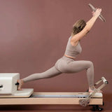 Elina Pilates Pilates-Ring in Taupe, Frau im Ausfallschritt auf dem Reformer hält den Ring über dem Kopf