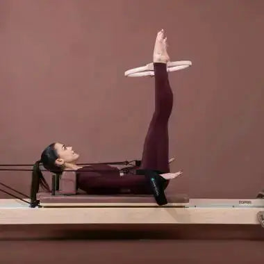 Elina Pilates Pilates-Ring in Rosa, Frau in Rückenlage auf dem Reformer mit dem Ring zwischen den Füßen