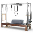 Elina Pilates Reformer Cadillac Klassisch Dunkles Holz – Schrägansicht mit Trapezstange und grauen Polstern
