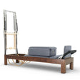 Elina Pilates Reformer Klassisch Dunkles Holz mit Tower, Schrägansicht mit grauen Polstern und dunklem Holzrahmen