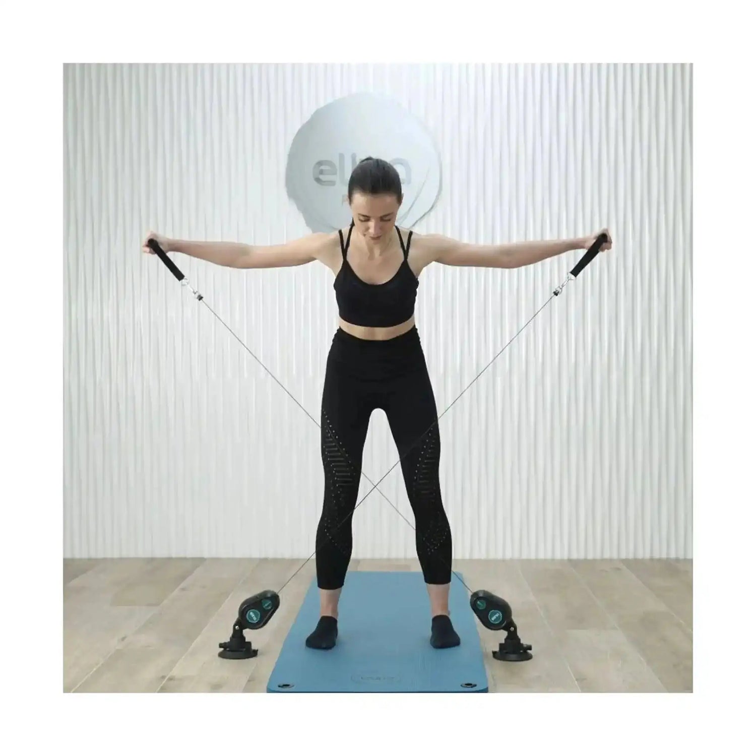 Frau steht mit seitlich gestreckten Armen und dem Elina Pilates Training Cord Widerstandstrainer