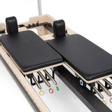 Elina Pilates Twin Reformer aus Ahornholz, Detail der beiden Wagen mit Schulterstützen und farbigen Federn